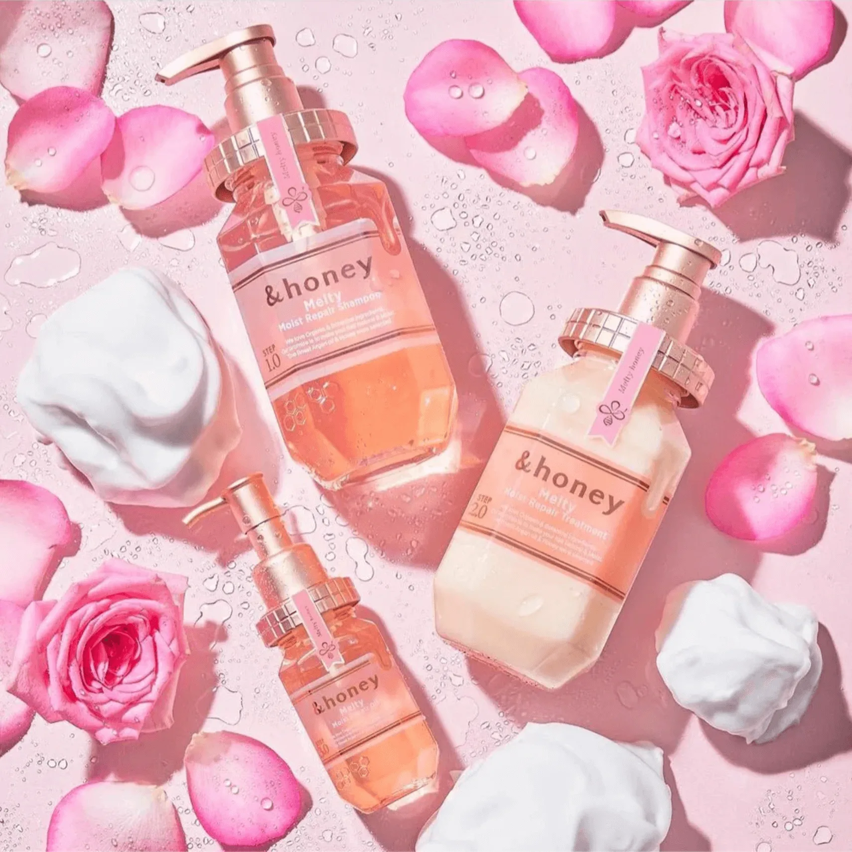 Three refillable hand soap bottles surrounded by pink roses, petals and foam on a pastel background.