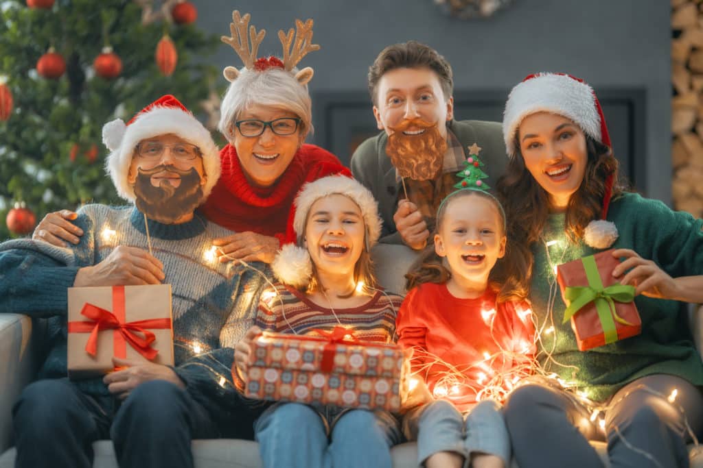 Merry Christmas and Happy Holidays. Grandma, grandpa, mum, dad and children exchanging gifts. Parents and daughters having fun near tree indoors. Loving family with presents in room.