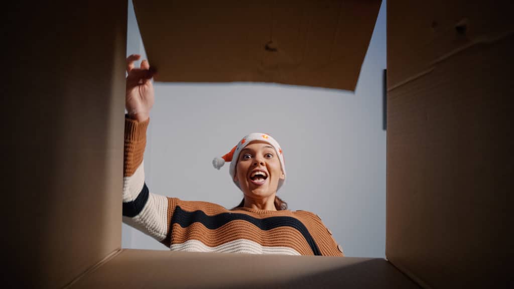 Festive woman unpacking box to reveal surprise at home. Young adult unwrapping gift smiling while checking package. Person with christmas spirit receiving present for holiday celebration