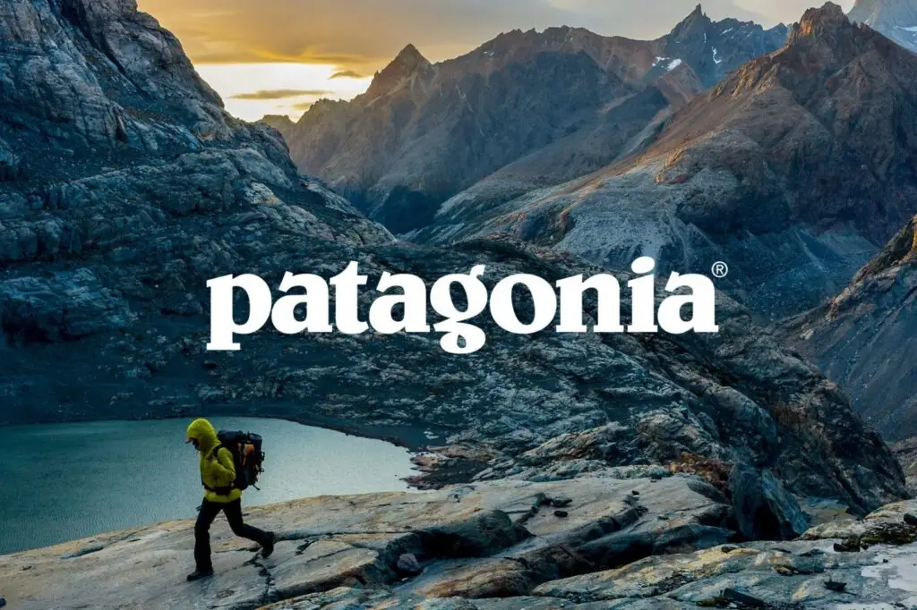 Hiker in yellow jacket explores rocky mountain terrain at sunrise with Patagonia logo overlay.