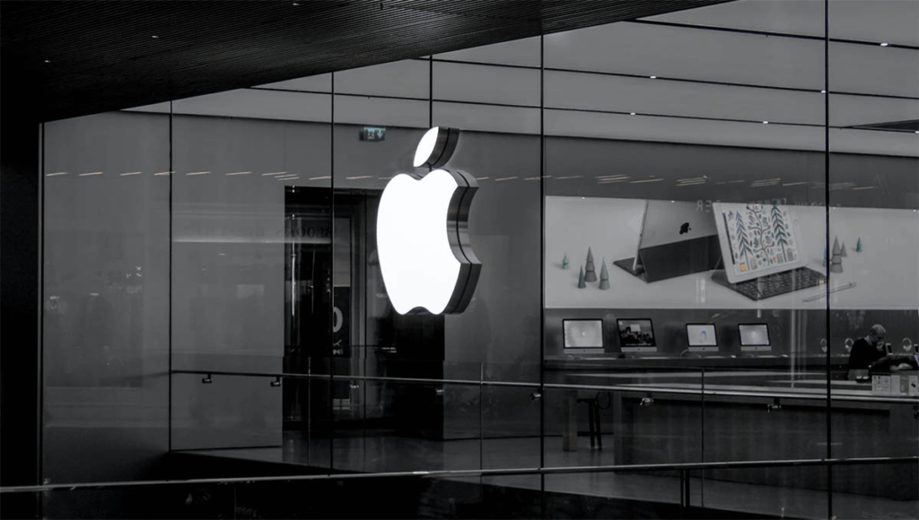 Large illuminated Apple logo on glass storefront with computers displayed inside.