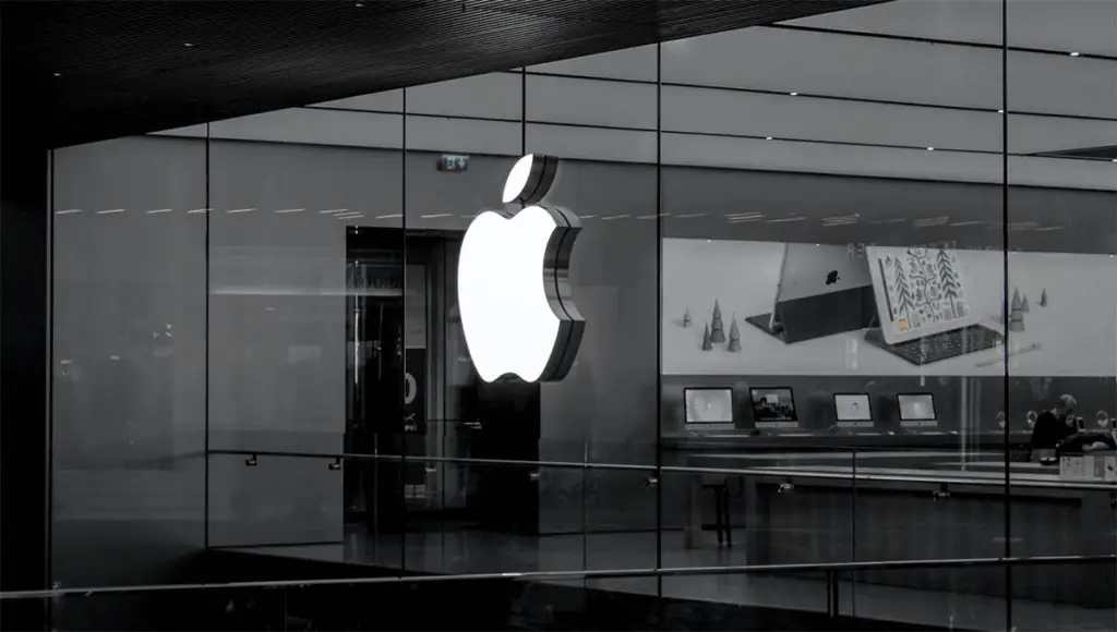 Large illuminated Apple logo on glass storefront with computers displayed inside.
