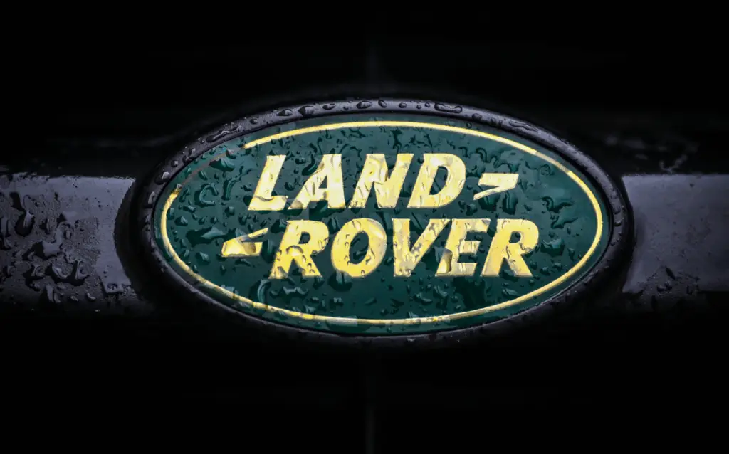 Land Rover badge with yellow text on green oval, covered in water droplets.
